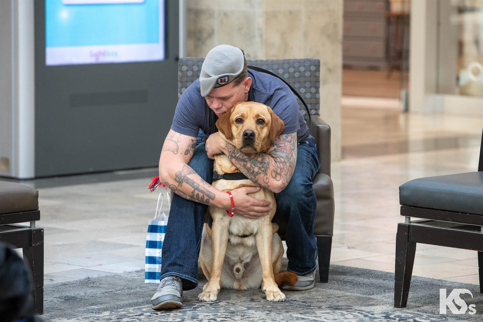 A Veteran hugging his yellow Labrador Service Dog while sitting together in a shopping center.